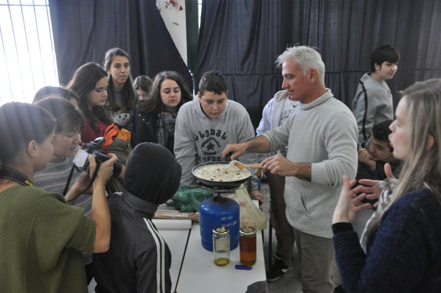 a group of tourists watching a man making honey-based superfoods on a camping gas in a pan at 'The Bear's Honey' and they take photos with a camera