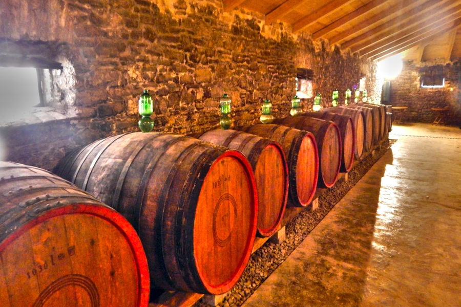 lying wine wood barrels in a row with gas lamps on the top of each one at 'Theotoky Estate' cellar