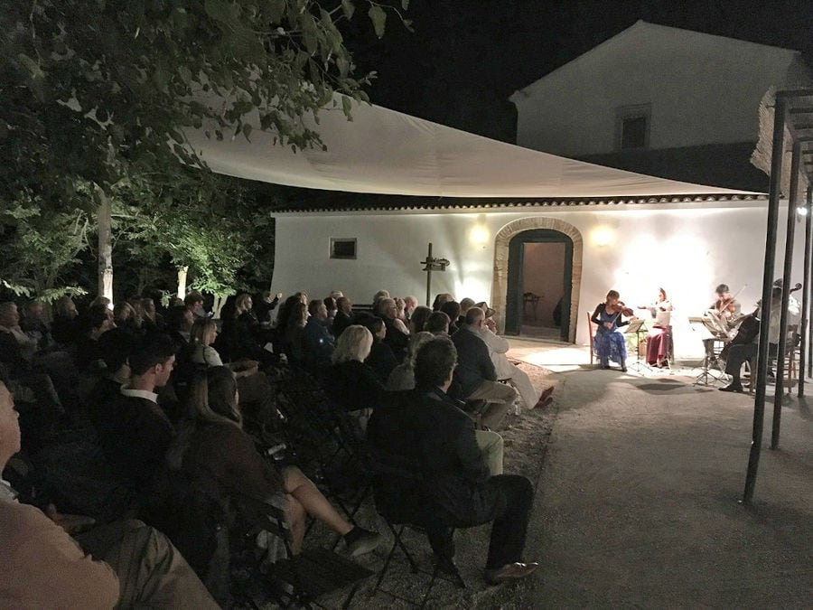 tourists sitting at 'Theotoky Estate' outside, listening to a concert by night