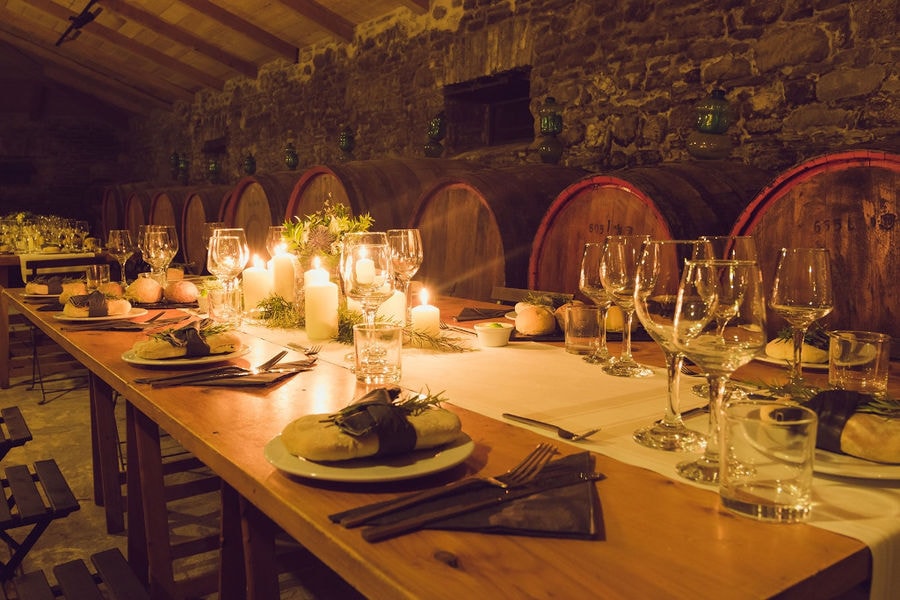 long wood table with glasses of wine and plates in front of lying wine barrels on the one side at 'Theotoky Estate' stone cellar
