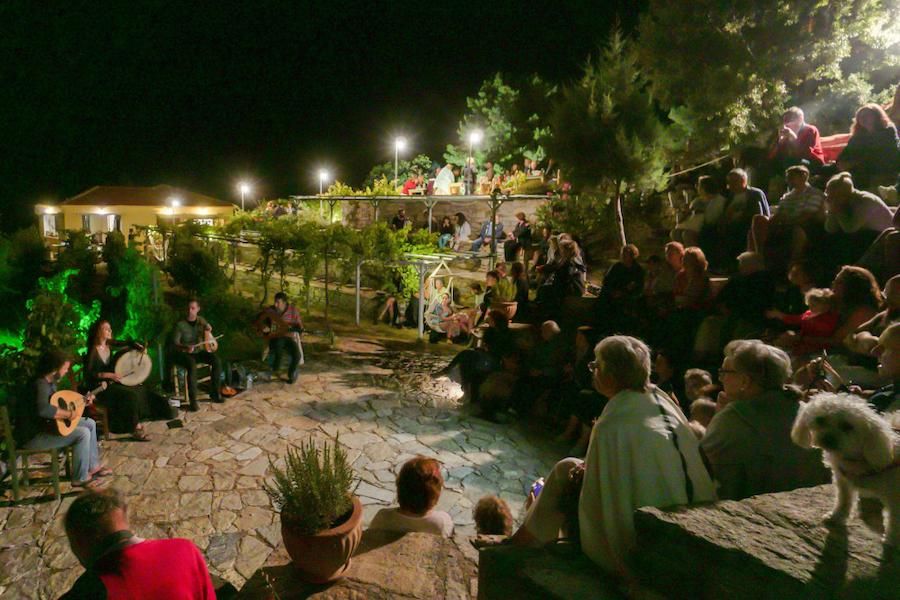 tourists sitting on stone amphitheater by night and listening the concert with traditional music instruments outside Afianes wines