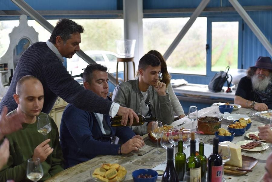 tourists sitting at the table, tasting wines inside at Domaine Dereskos winery and listening a guide