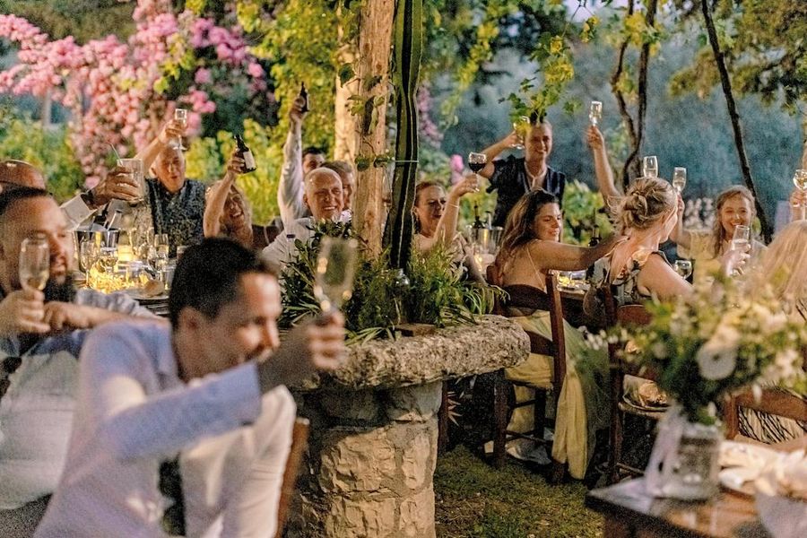 tourists smiling and raise their glasses of wine for 'cheers' at illuminated Dourakis Winery garden by night