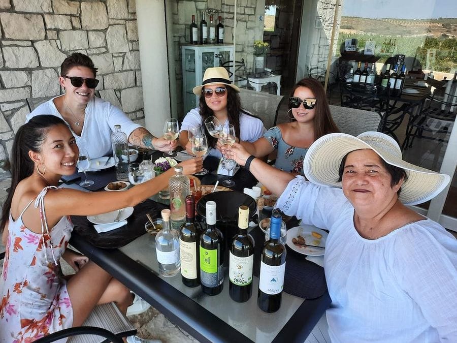 tourists smiling at the camera and holding glasses of wine for 'cheers' and eating aperitifs at Domaine Paterianakis winery