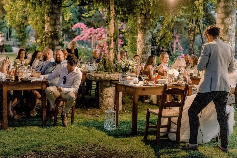 tourists standing in the illuminated garden of Dourakis winery, tasting wines and listening to a guide