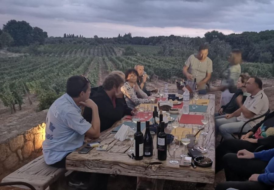 tourists sitting at the table, tasting wines outside at Domaine Dereskos vineyards and listening a guide