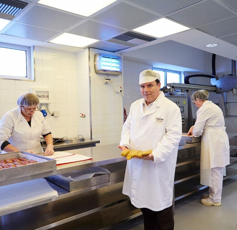 man holding bottarga smoking and watching and showing them at the camera at Trikalinos plant