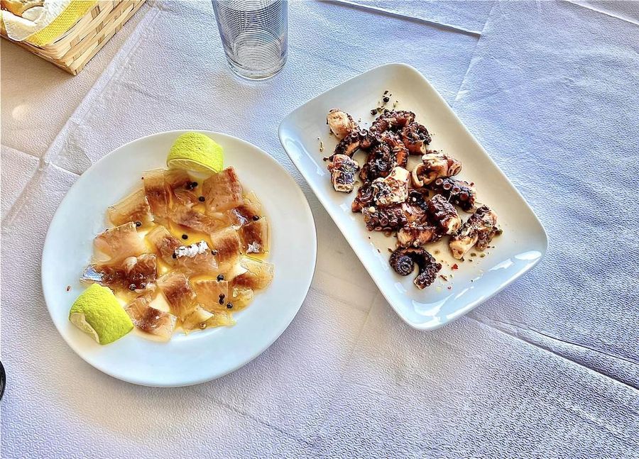 view from above of two plates with roasted octopus and fillet of fish marinated in oil with pieces of lemon of lemon from Stefanos Kaneletis