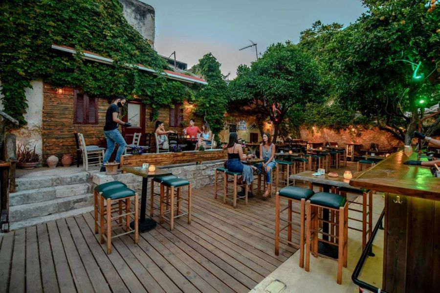 A cozy bar in Crete, its wooden floor lending warmth, as numerous chairs and tables invite patrons to gather, indulge, and savor the vibrant atmosphere of the island.