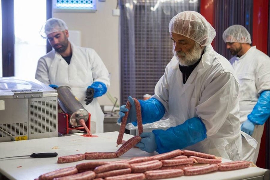 three men workers at Vavourakis Farm workshop one of them stuffing sausage and the other putting them on white table