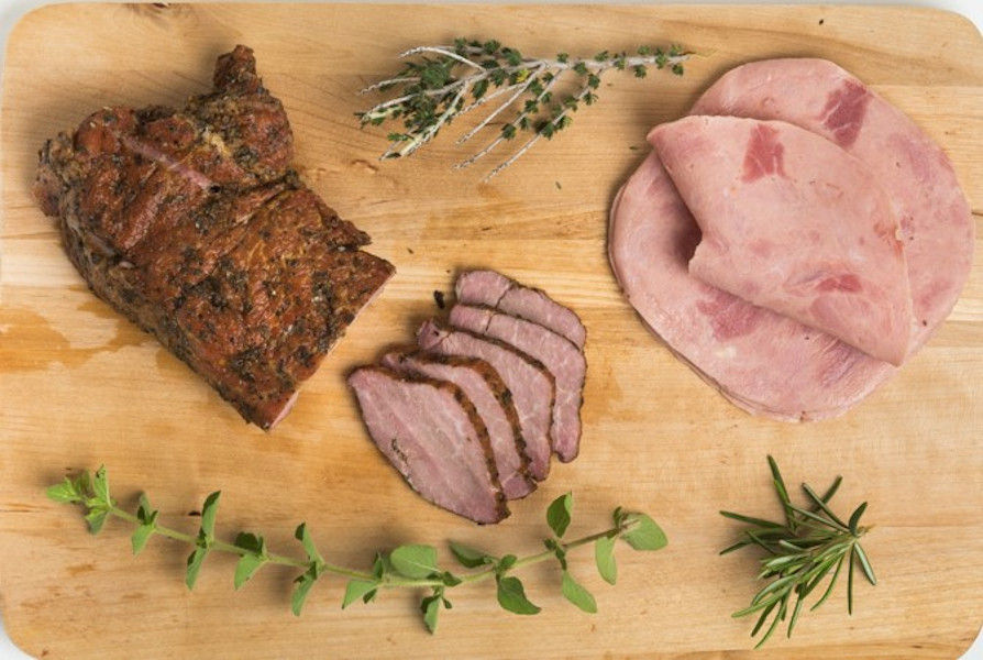 close-up of pieces of processed meat, singlino, apaki, ham and fresh herbs on wooden tray at Vavourakis Farm