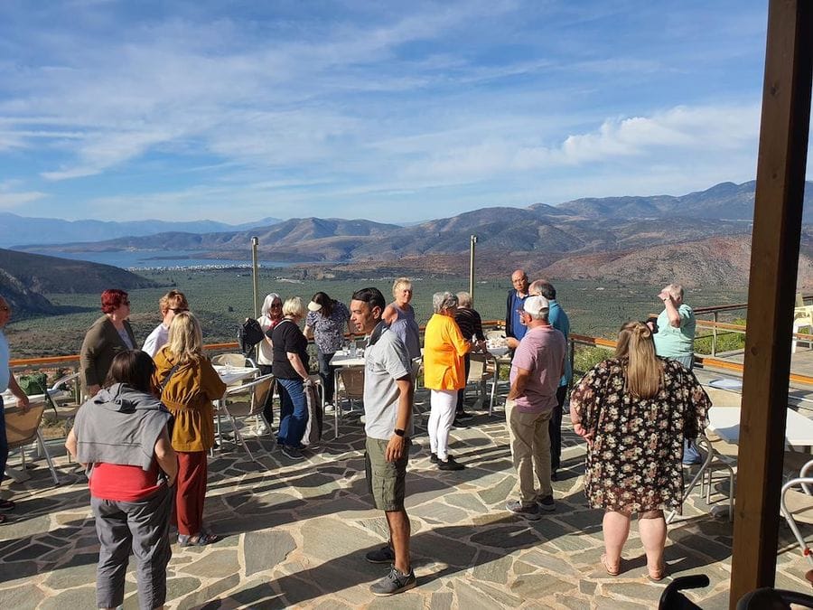 visitors listening to a guide at Mer des Oliviers de Delphes and mountains and olive groves in the background