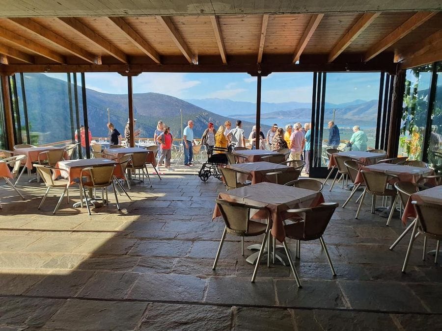 visitors outside of the terrace of Mer des Oliviers de Delphes with tables and chairs, mountains and olive groves in the background