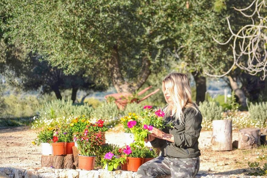 woman holding purple flowers and sitting by the flower pots at olive grove En Kefallinia Organic Farm Restaurant