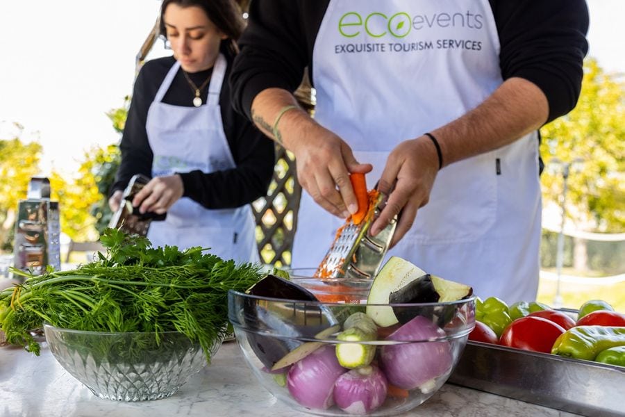 Two people grate vegetables with a grater, their focused expressions and swift movements transforming fresh produce into fine shreds. Bowls brimming with an array of vibrant vegetables await, ready to be incorporated into a wholesome culinary creation.