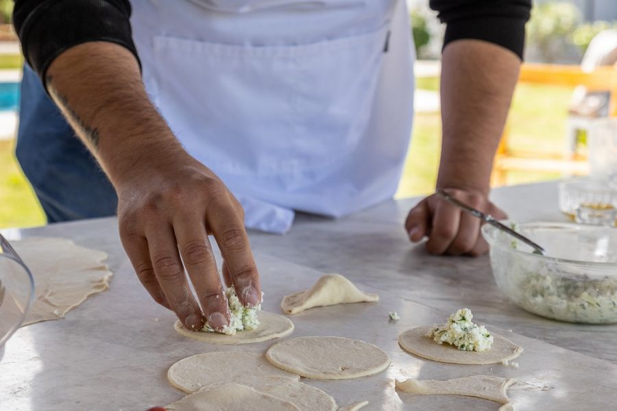 A man meticulously fills small pieces of dough with cheese, his hands working with precision and care, ensuring each parcel is a delectable burst of cheesy goodness waiting to be savored.