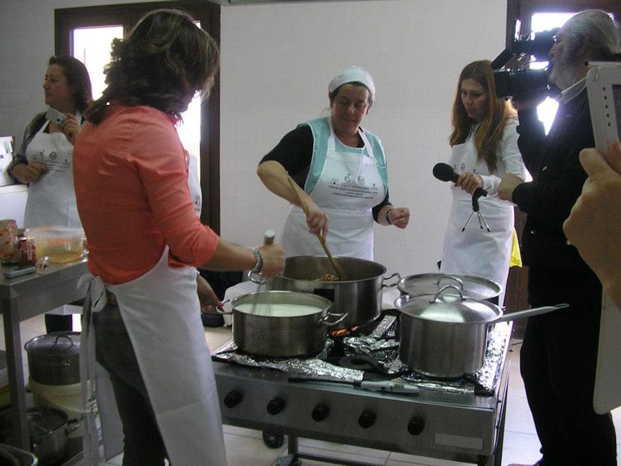 women cooking and mixing in cooking pots and a man taking video with the camera at workshop