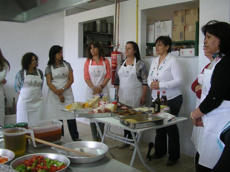 women around the short tables with cooking foods and watching at the camera