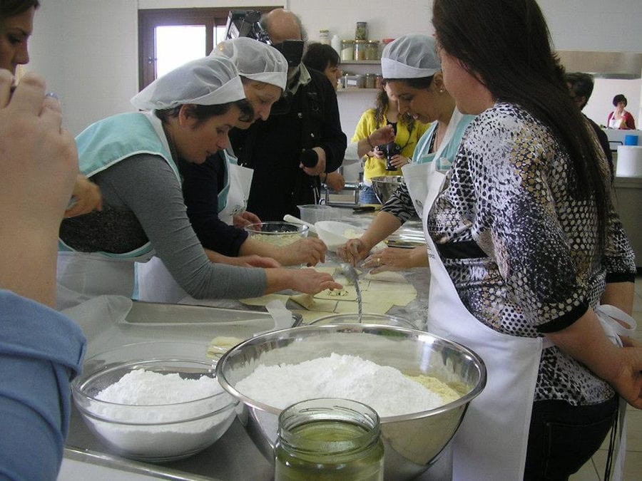 women cooking pies with flour and a man taking video with the camera at 'Agrotouristic Women's Cooperative of Mesotopos Lesvos' workshop