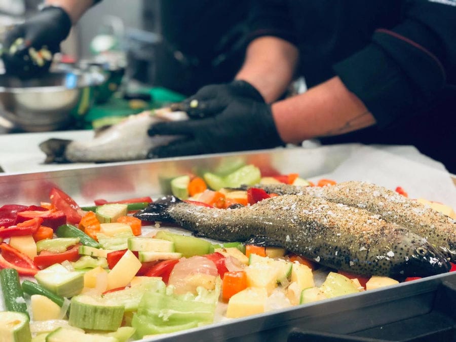 man adding salt to fresh fish and then putting it in the was with vegetables at 'Pitenis' plant