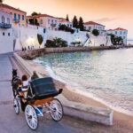 A horse-drawn carriage glides along the sandy beach, with gentle waves lapping at the shore in the background.