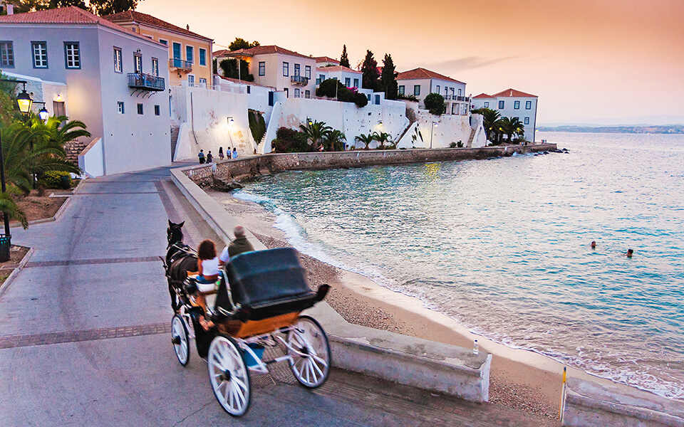 A horse-drawn carriage glides along the sandy beach, with gentle waves lapping at the shore in the background.