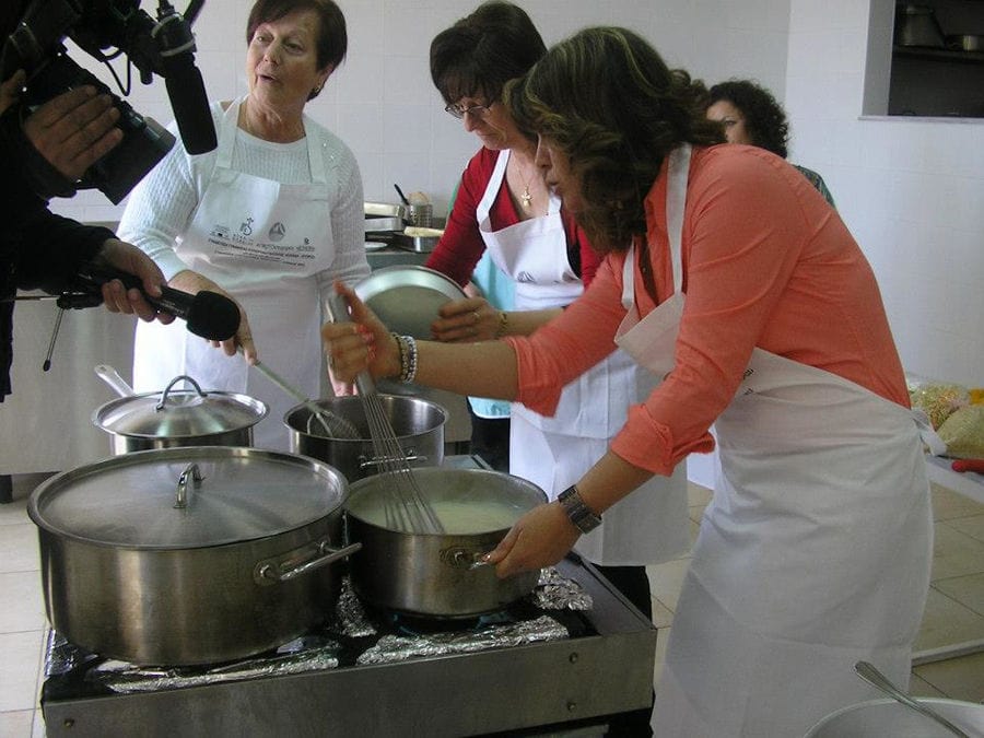 women cooking and mixing in cooking pots and a man taking video with the camera at workshop