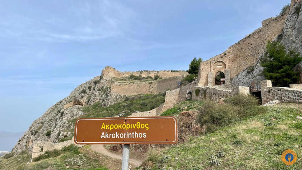 a sign on a hill with a stone building in the background