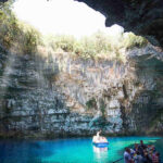 A small boat navigates the vibrant blue waters within a cave, highlighting the natural beauty of the surrounding rock walls.