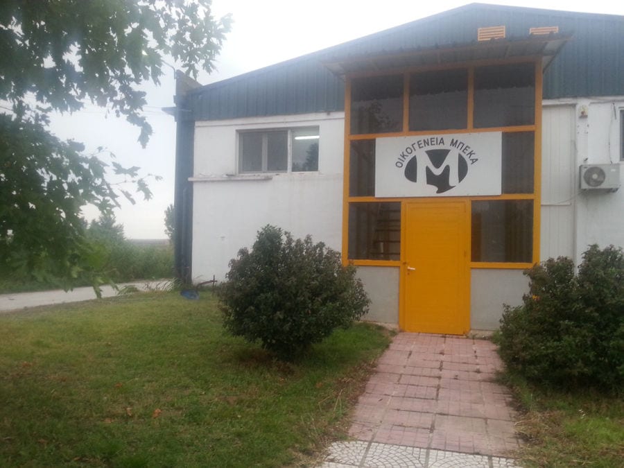 front view of entrance of 'Bekas Family Farm' building plant surrounded by green bushes and grass