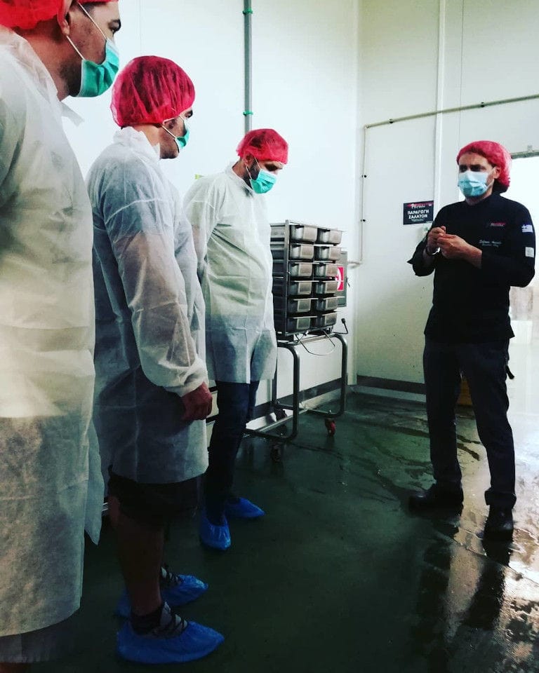 a group of tourists listening to a man giving a tour at 'Pitenis' plant and everyone wears masks on their mouths